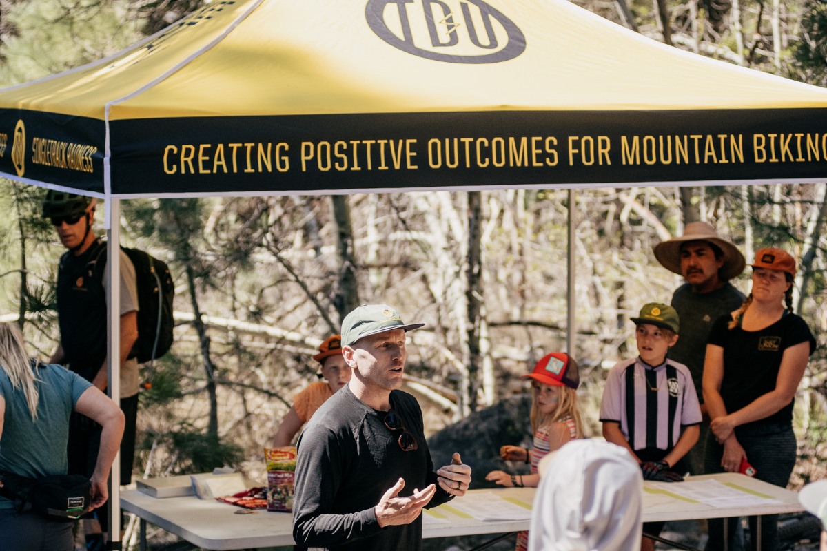 TDU tent with speaker talking to a crowd at a trail work day.