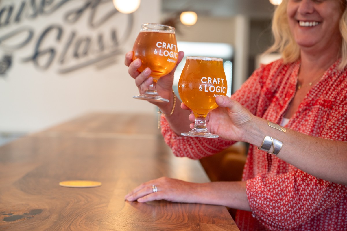 Two women lifting Craft and Logic glasses in a cheers.