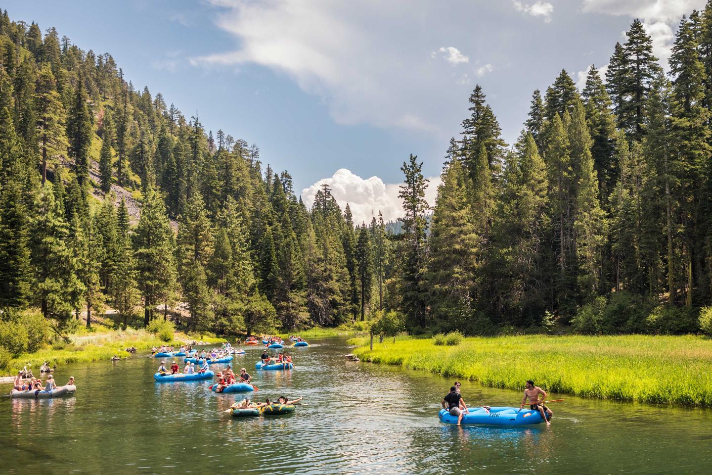 People floating on rafts down a river in a forested landscape under a partly cloudy sky.
