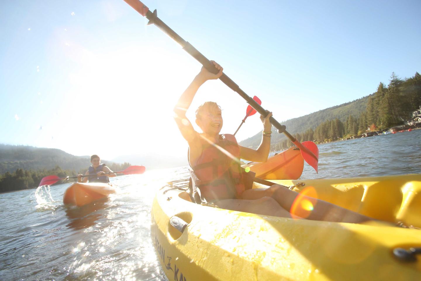 Child kayaking on a sunny lake, bright yellow kayak, joyful expression.