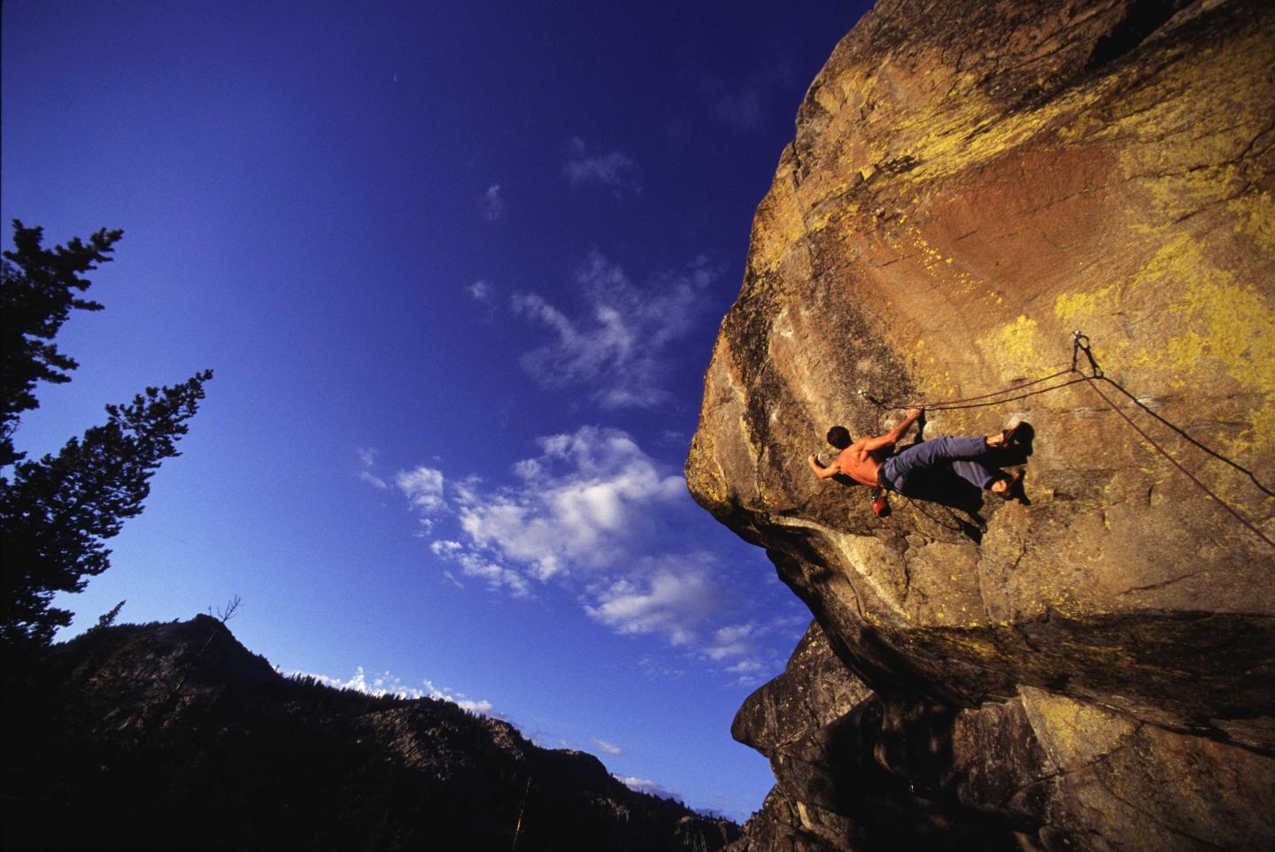 Rock climber on a large cliff against a deep blue sky.