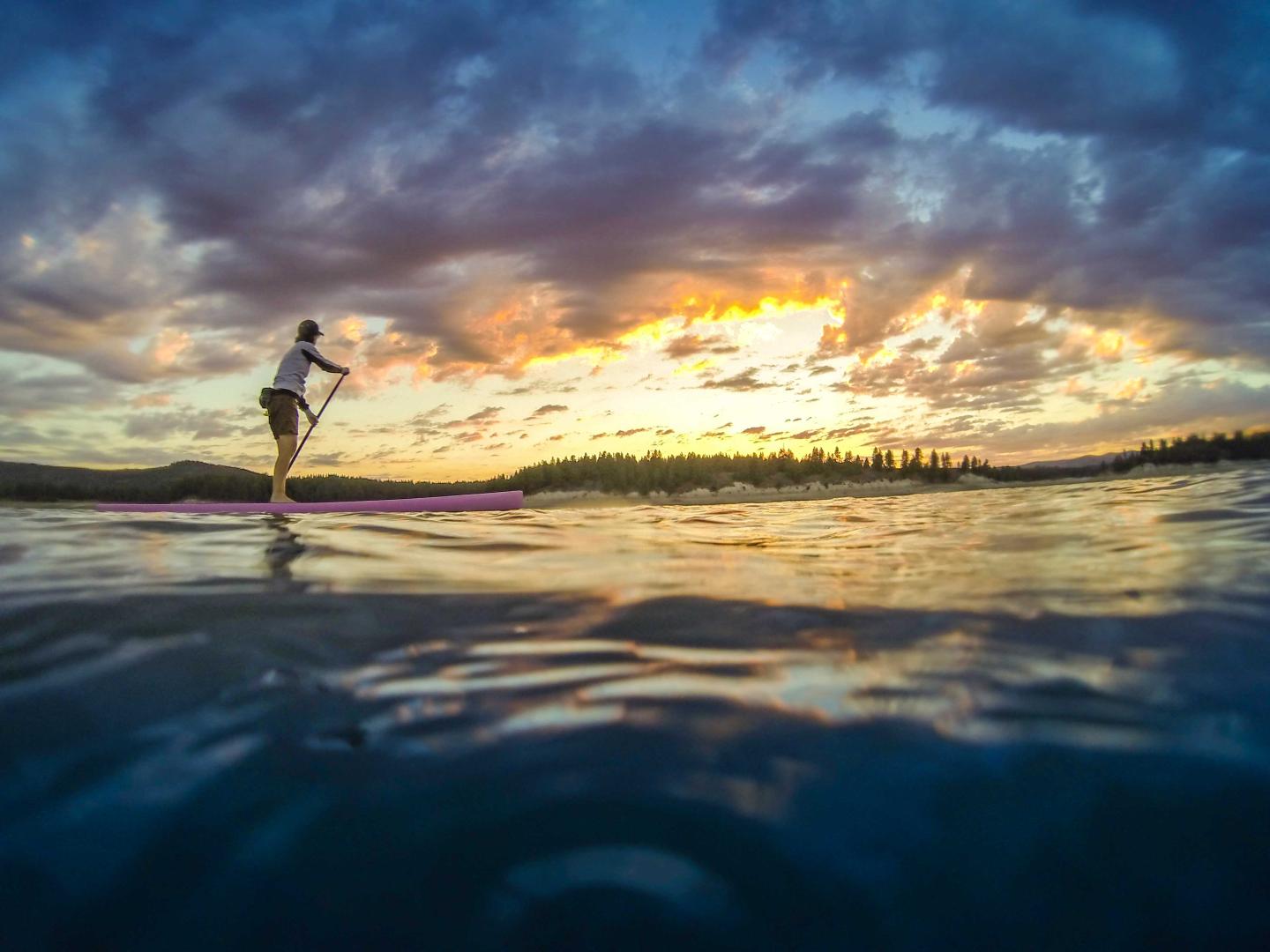 Paddleboarder on water at sunset with colorful clouds in the sky.
