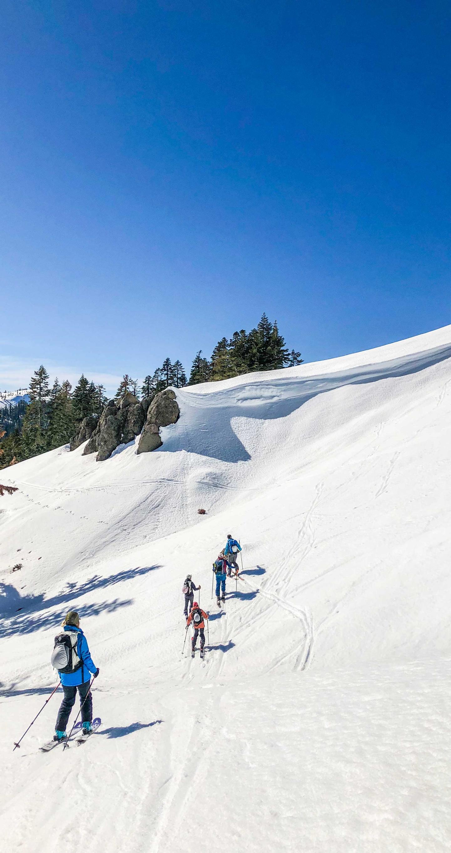Skiers descending a snowy slope under a clear blue sky.