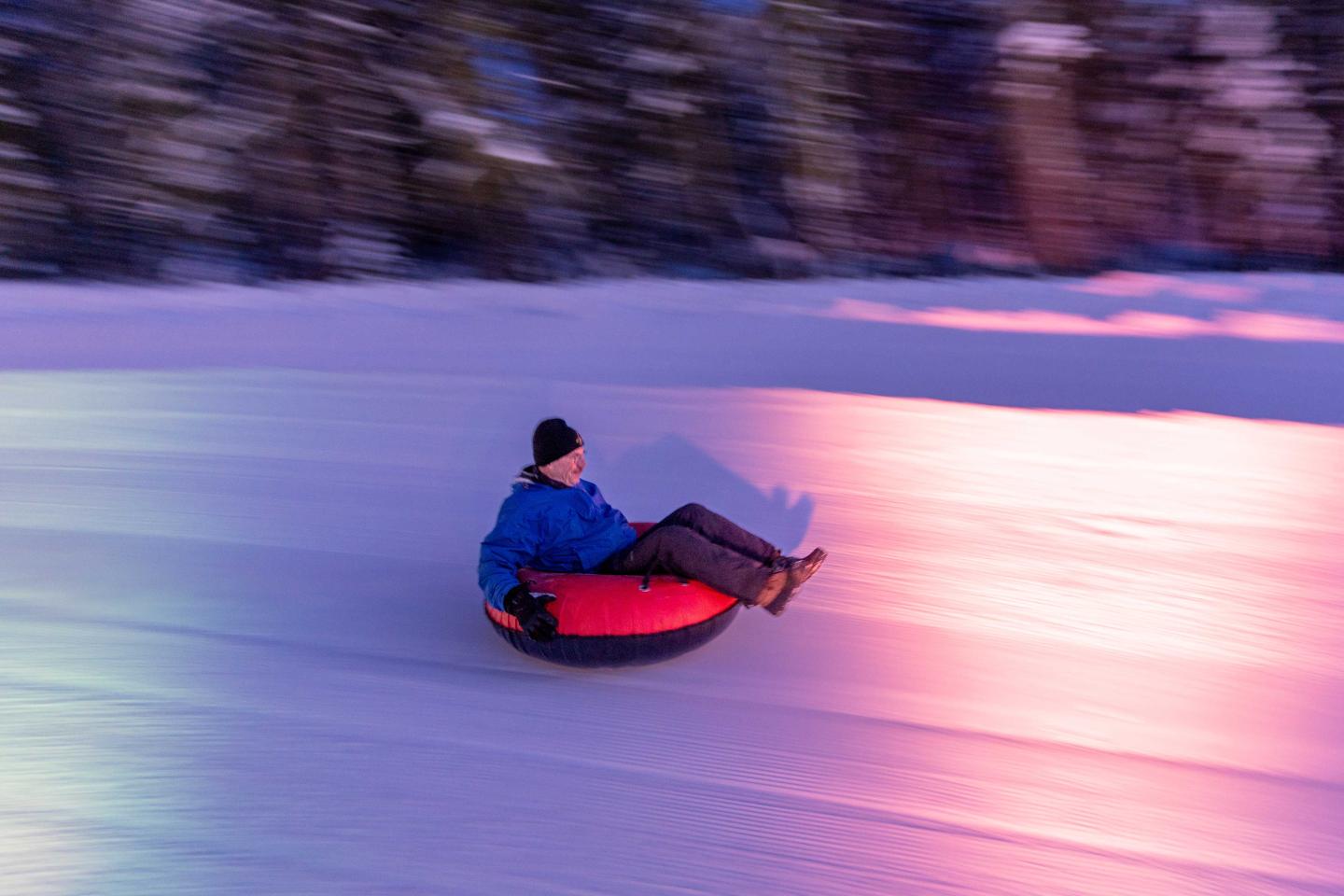 Person tubing on snow, colorful lights in motion blur.