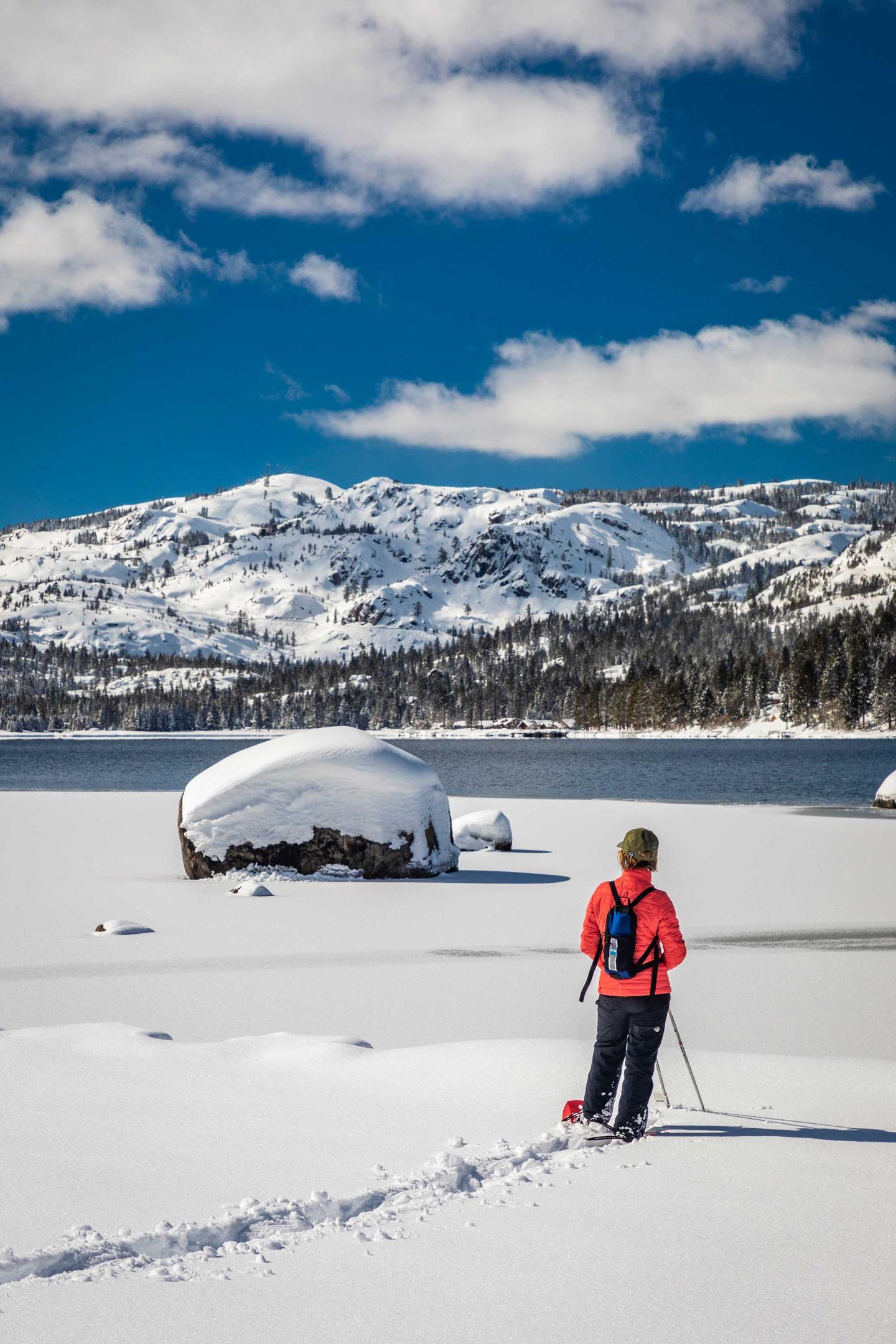 Person in red skiing across a snowy landscape with mountains and blue sky.