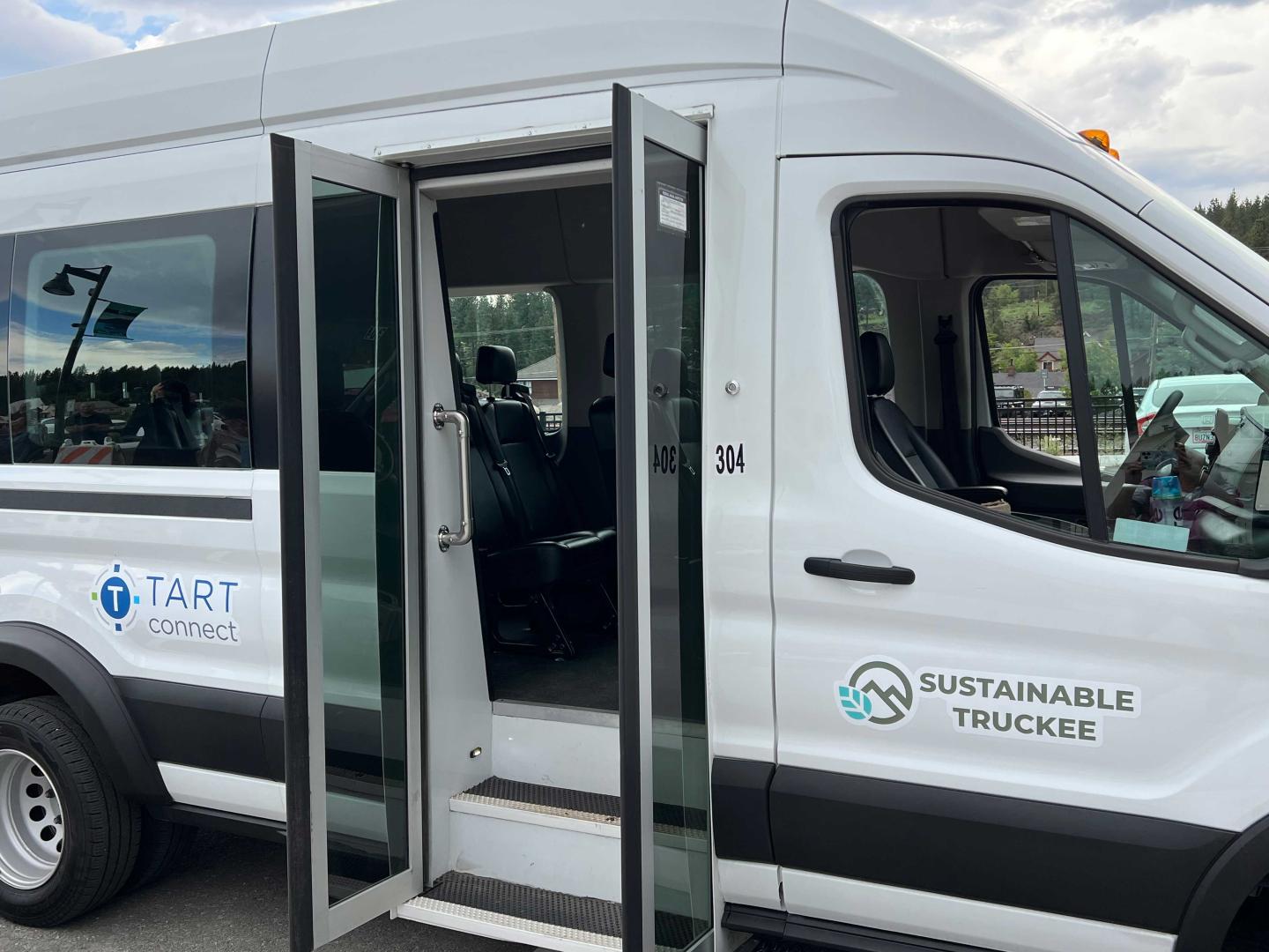 White shuttle van with open sliding door, branding for TART Connect and Sustainable Truckee.