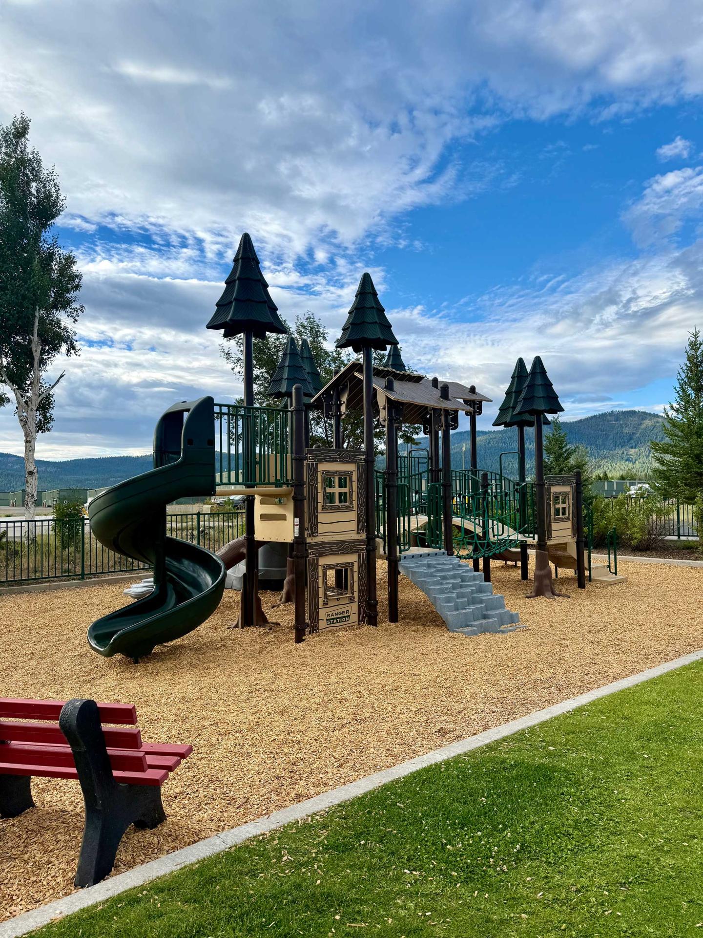 Playground with slides and climbing frames, set in a park under a blue sky.