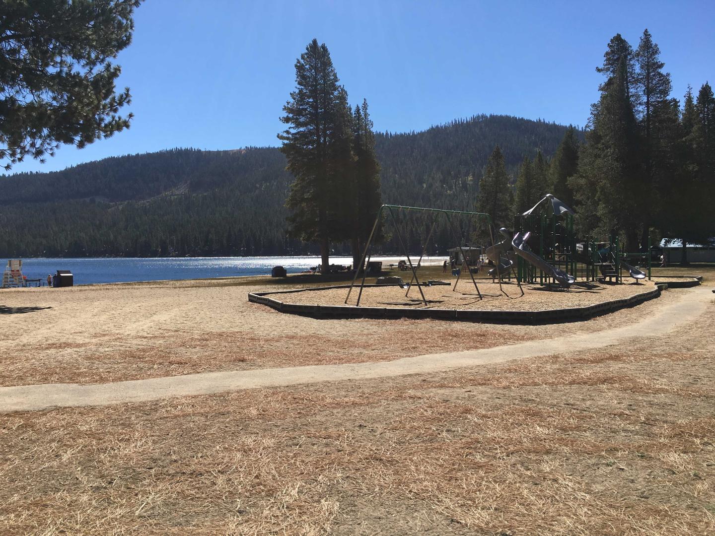 A lakeside playground with trees and mountains in the background.