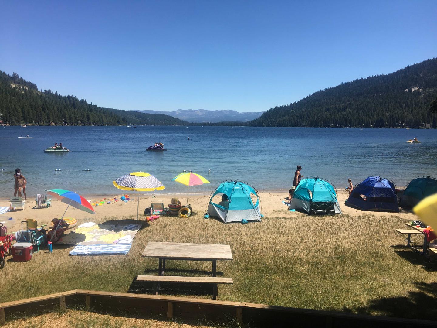 Beach with colorful umbrellas and tents by a lake under a clear blue sky.