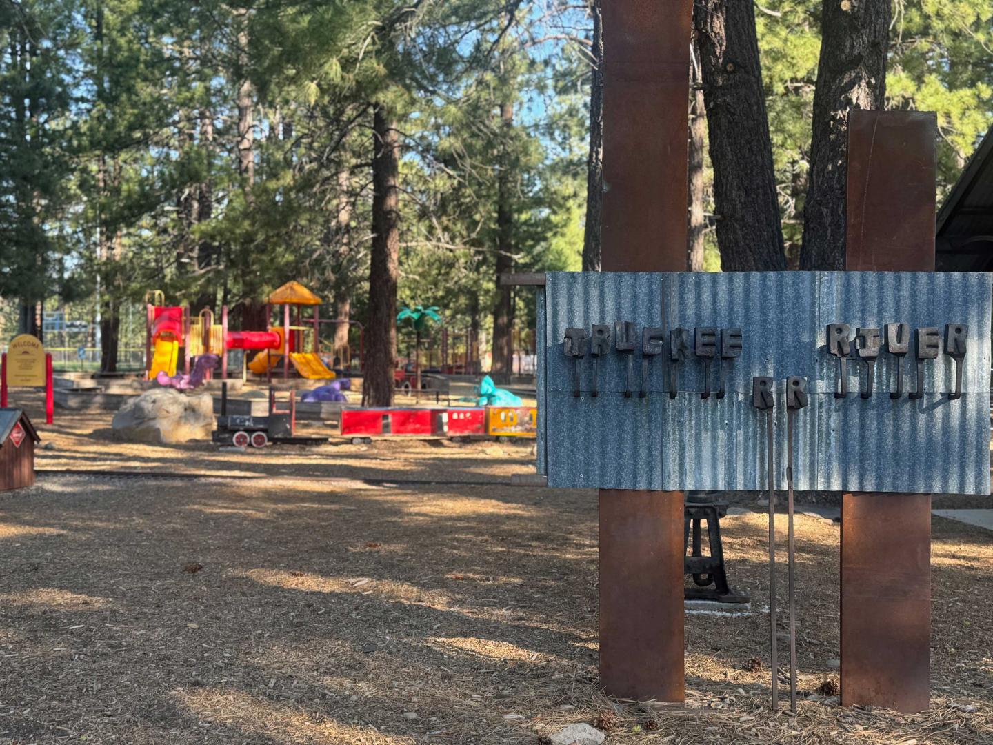 Playground among tall trees with colorful equipment, sunny day.