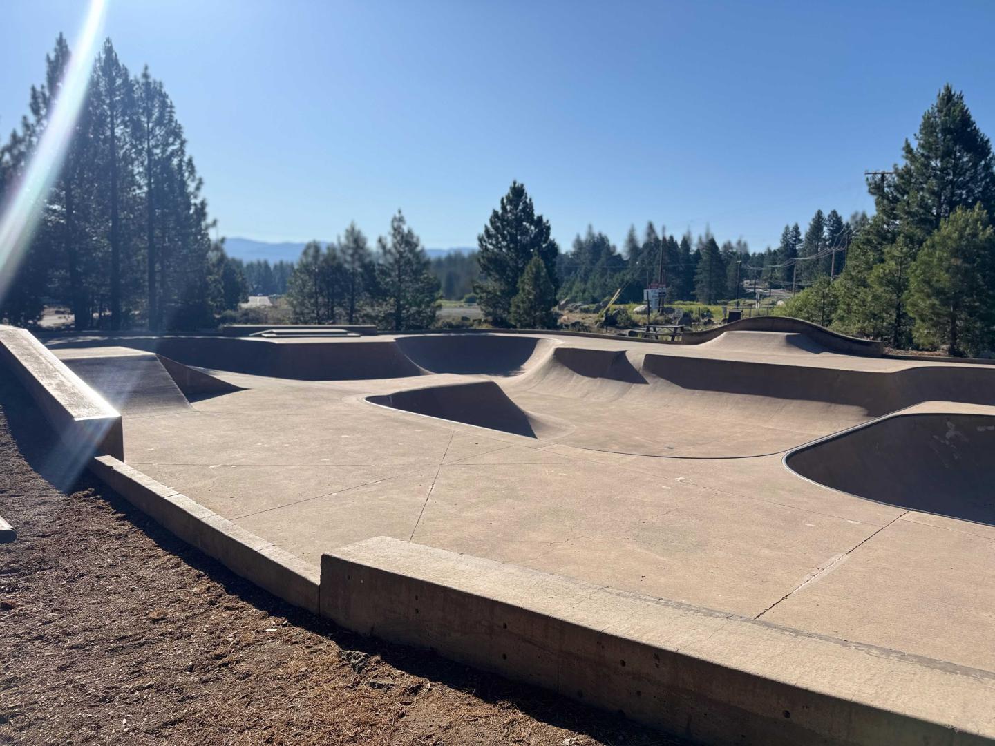 Concrete skate park under a clear blue sky, surrounded by trees.