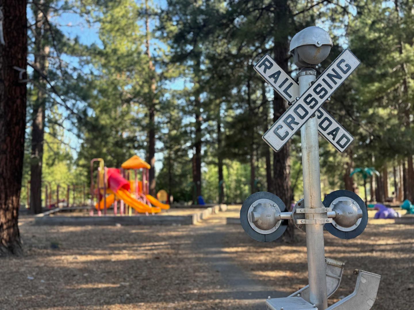 Playground with trees and a rail crossing sign in the foreground.