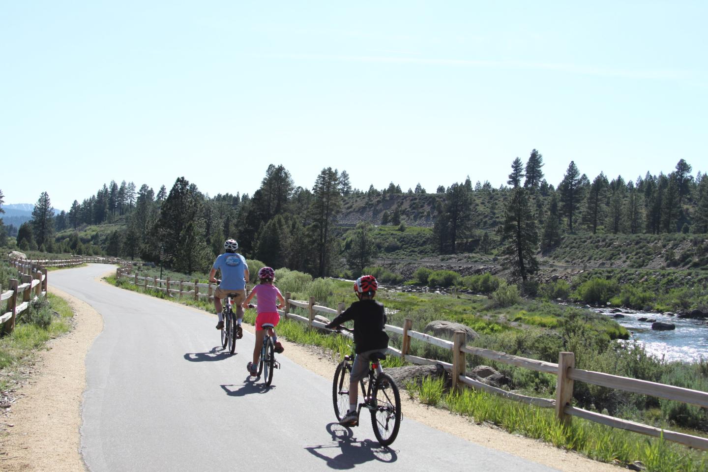 Cyclists on a paved path by a scenic river and forest.