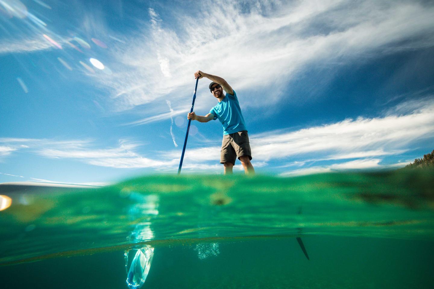 Man paddleboarding on clear water under a blue sky.