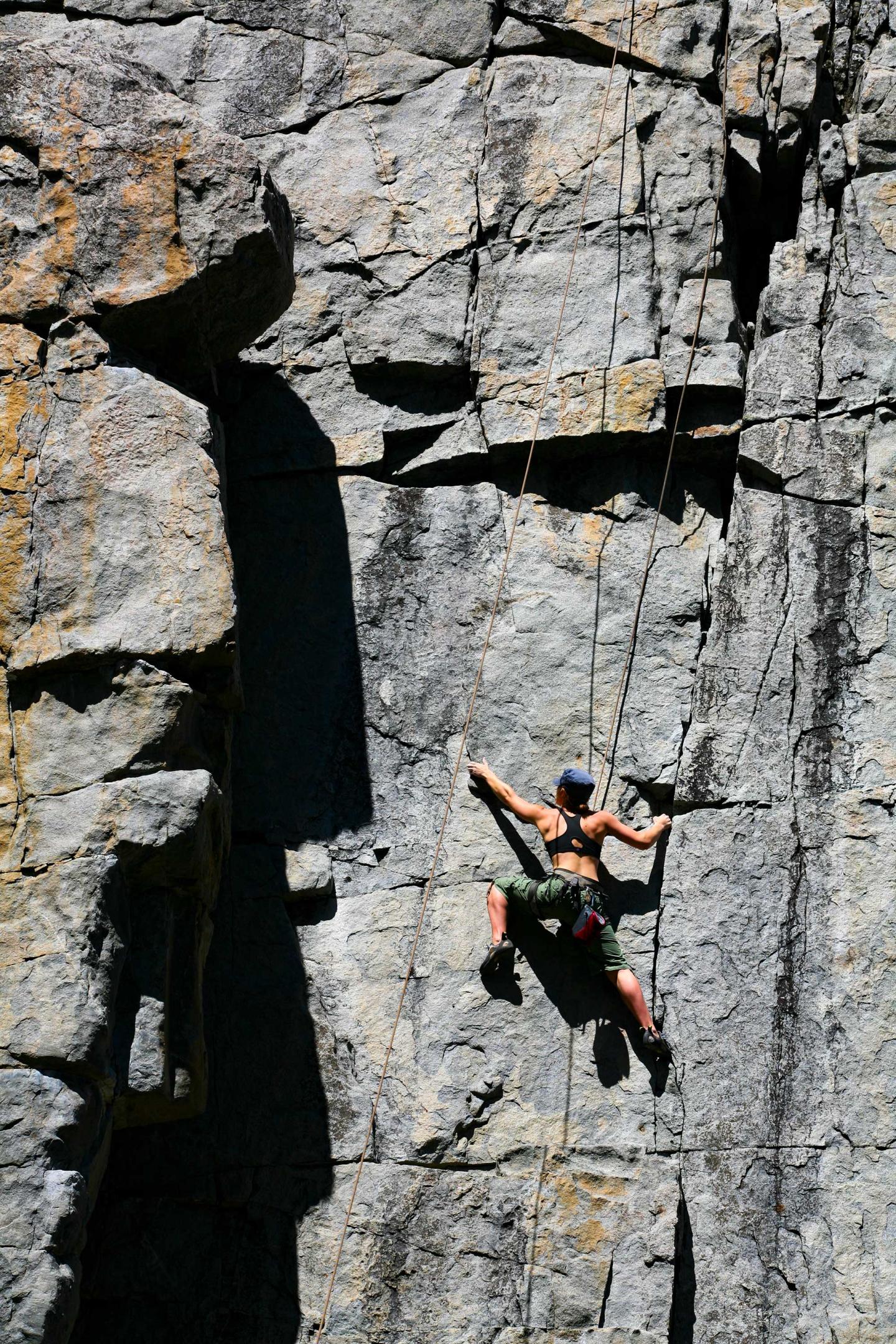 Rock climber scaling a steep, sunlit cliff face.