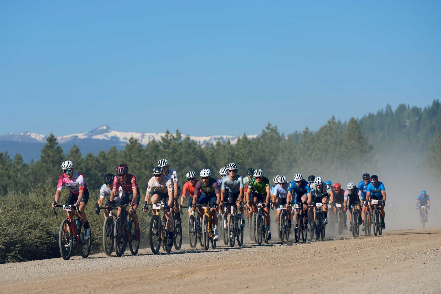 Cyclists racing on a dusty road with mountain backdrop.