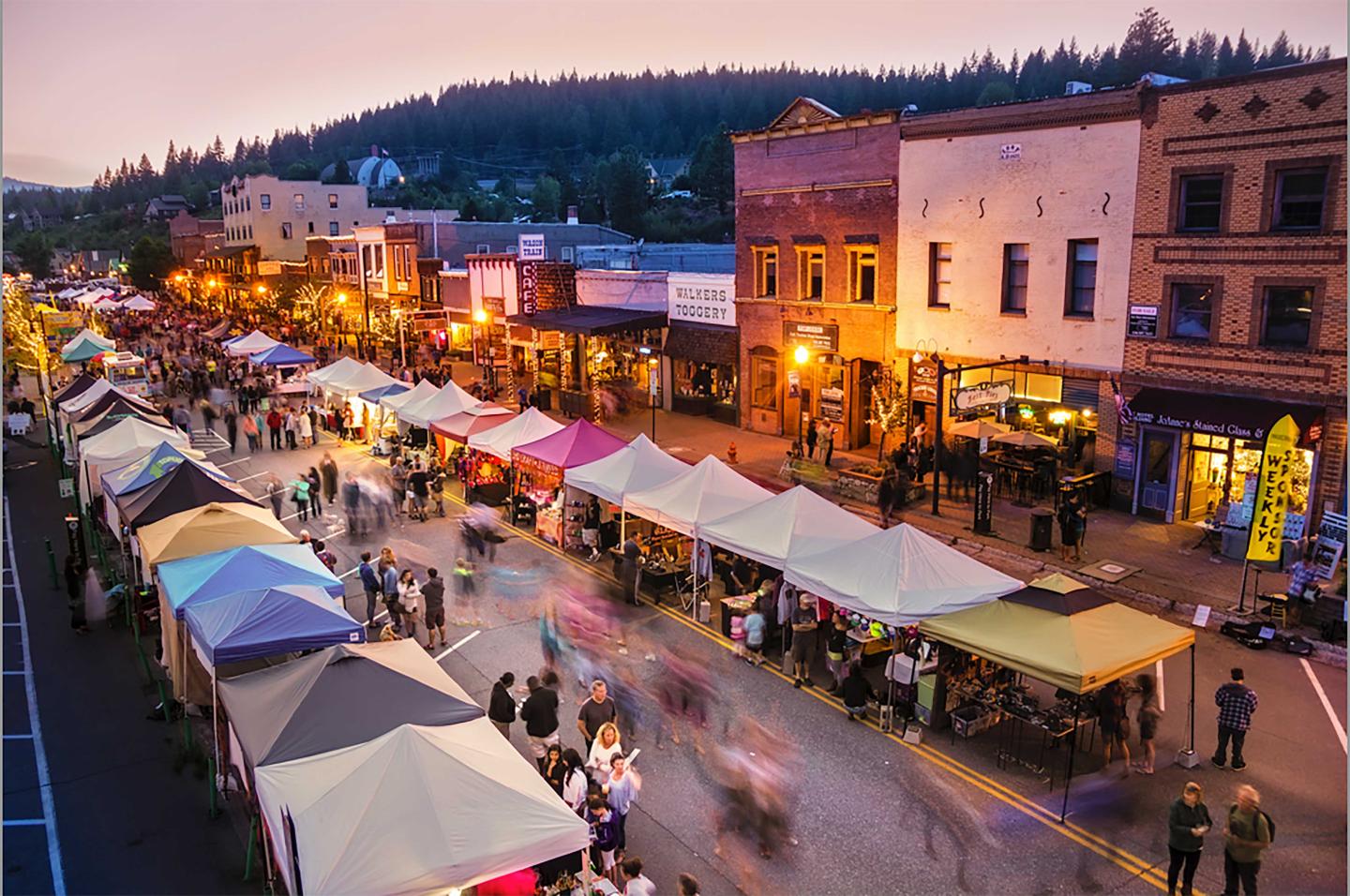 Street market with colorful tents and bustling crowd at dusk.