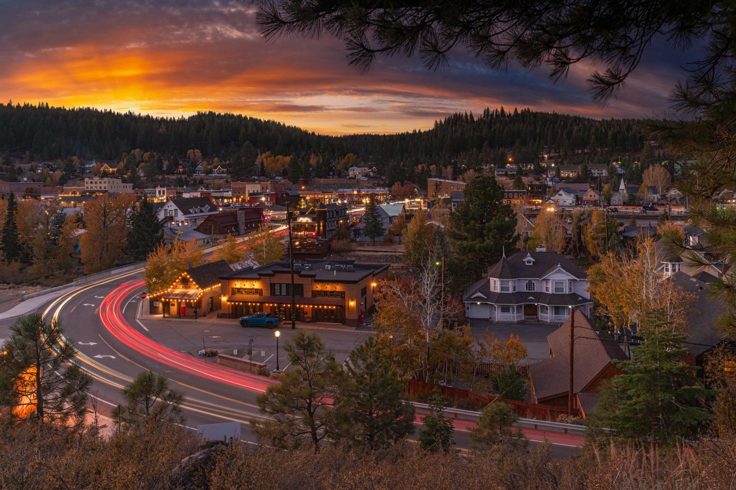 Sunset over a small town with car light trails on a winding road.