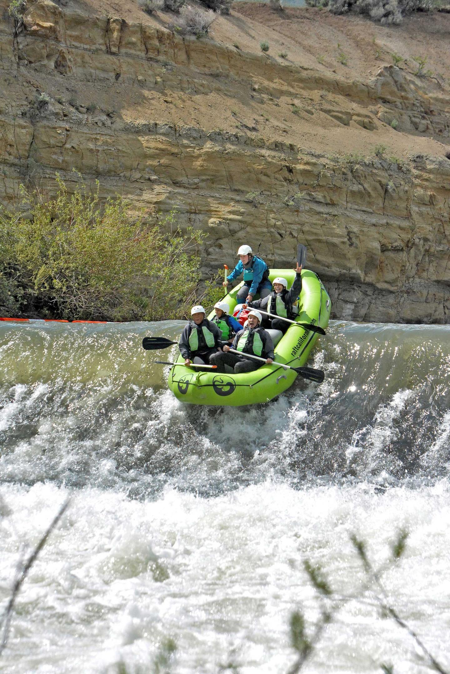 Raft with four people navigating a small waterfall.