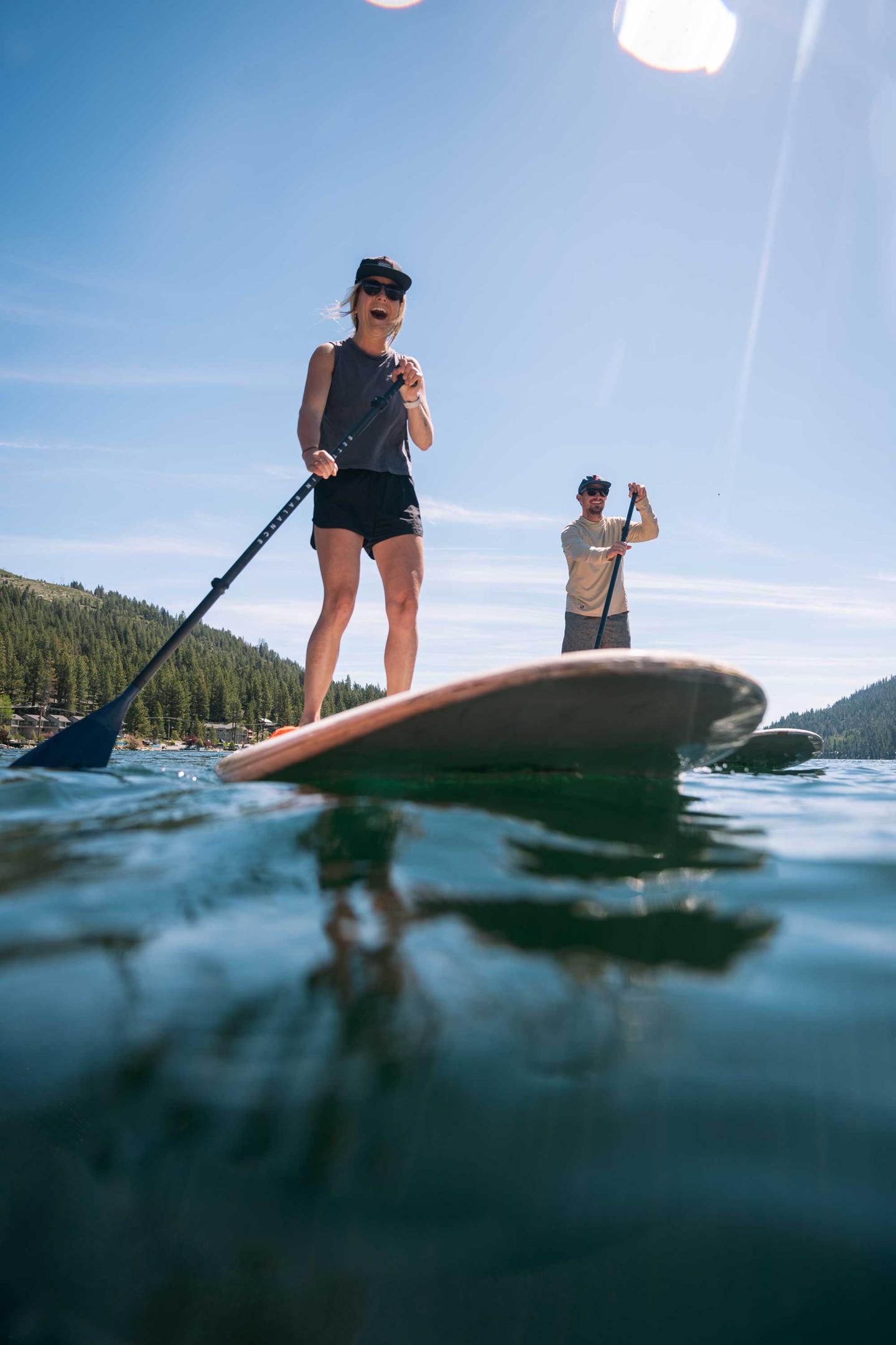 Two people paddleboarding on a lake under a clear blue sky.