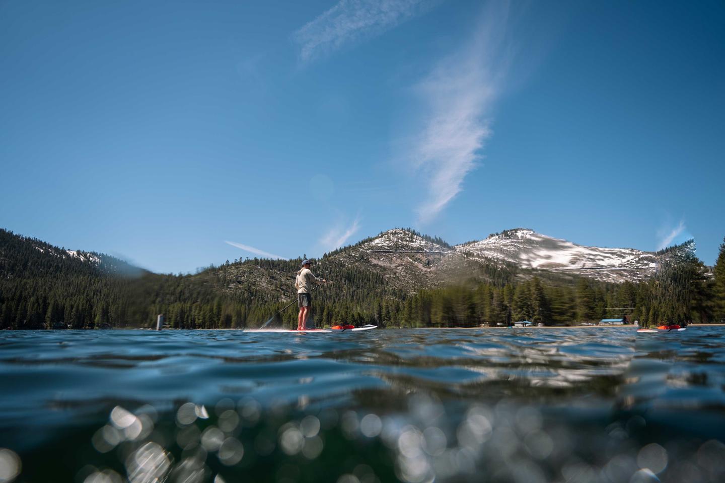 Paddleboarder on a lake with mountains in the background, under a clear blue sky.