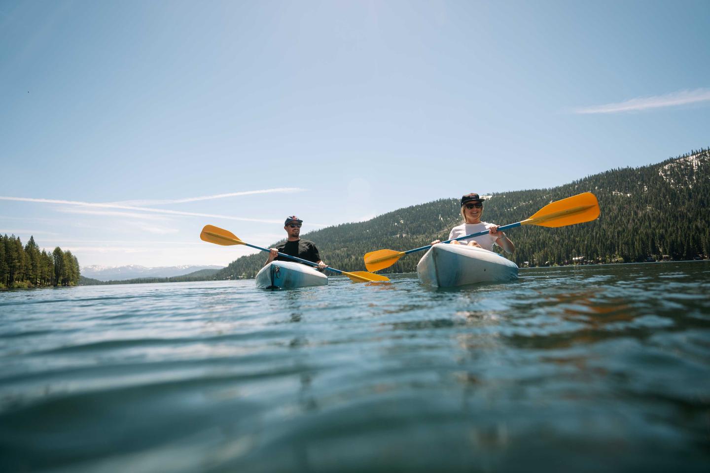 Two people kayaking on a lake under a clear blue sky.