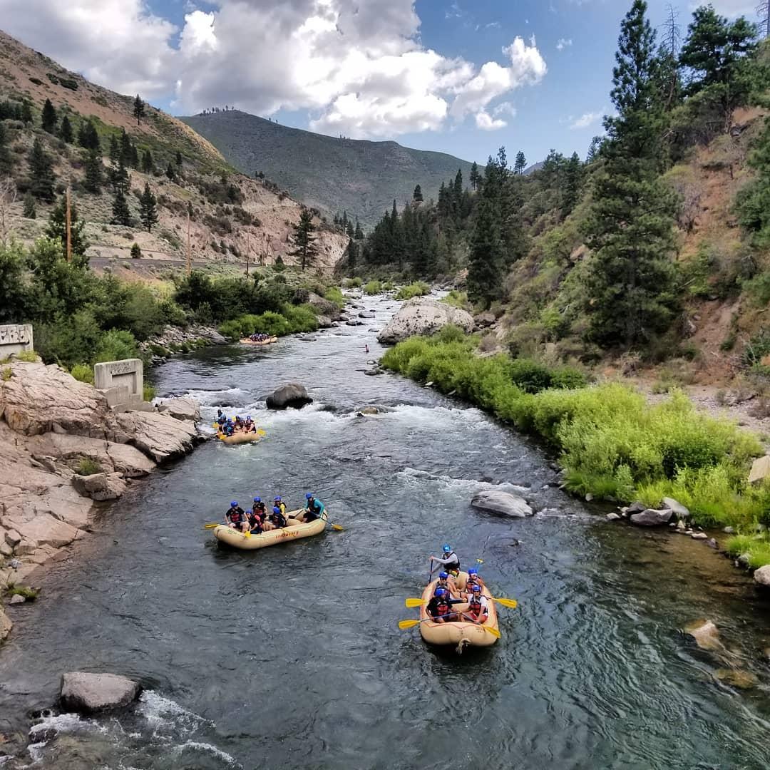 Rafts on a scenic river surrounded by trees and mountains under a cloudy sky.