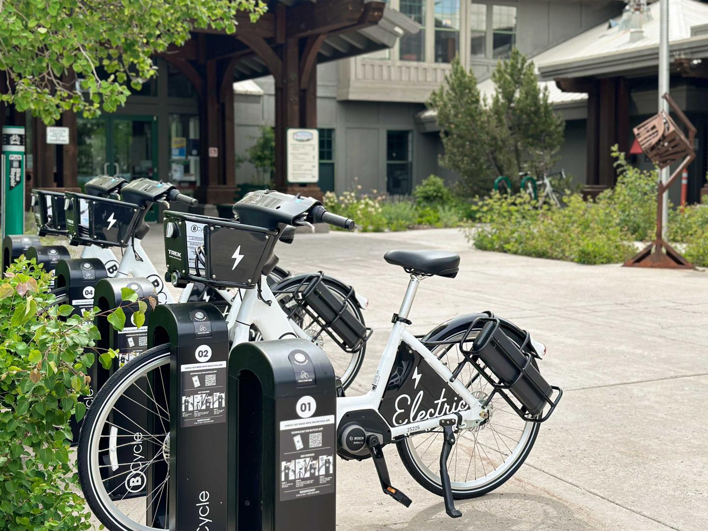 Electric bikes parked in a row at a charging station near a building.