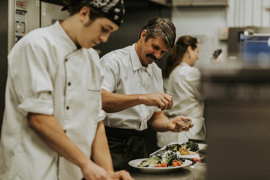 Chefs in a kitchen, preparing plates of food.