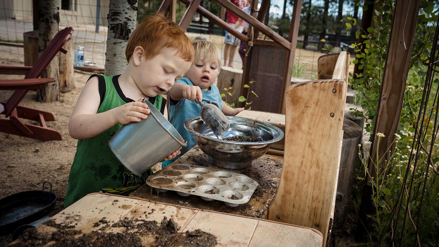 Children playing with dirt and water at an outdoor mud kitchen.