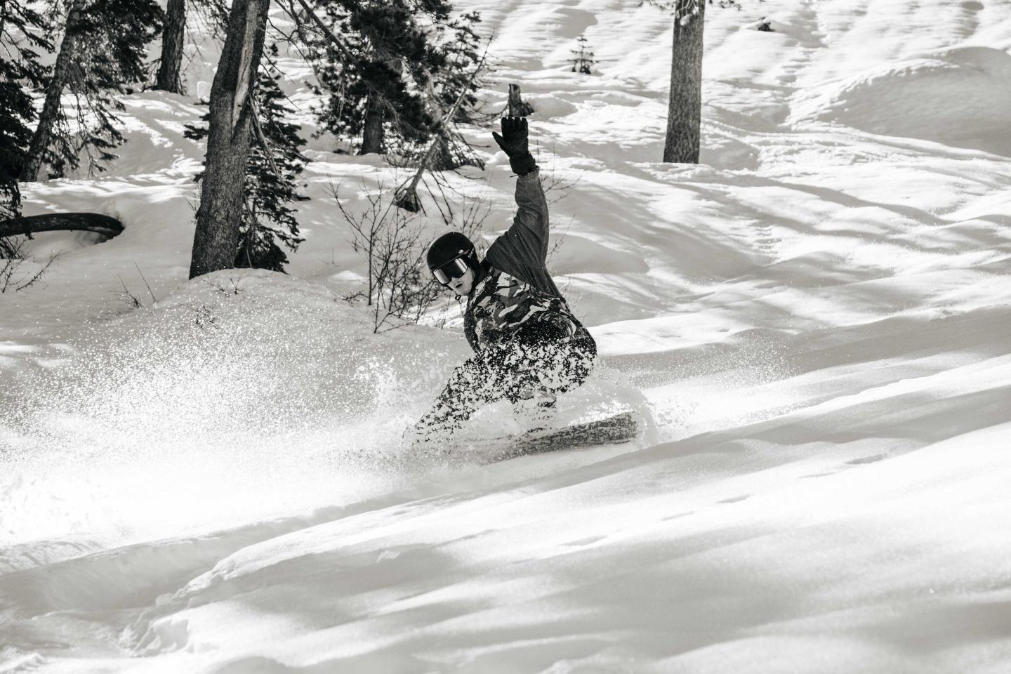 Snowboarder gliding down a snowy slope, surrounded by trees.