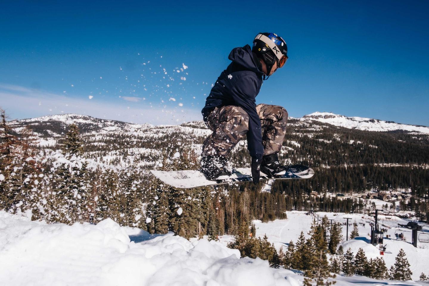 Snowboarder jumping off a snowy hill with mountains in the background.