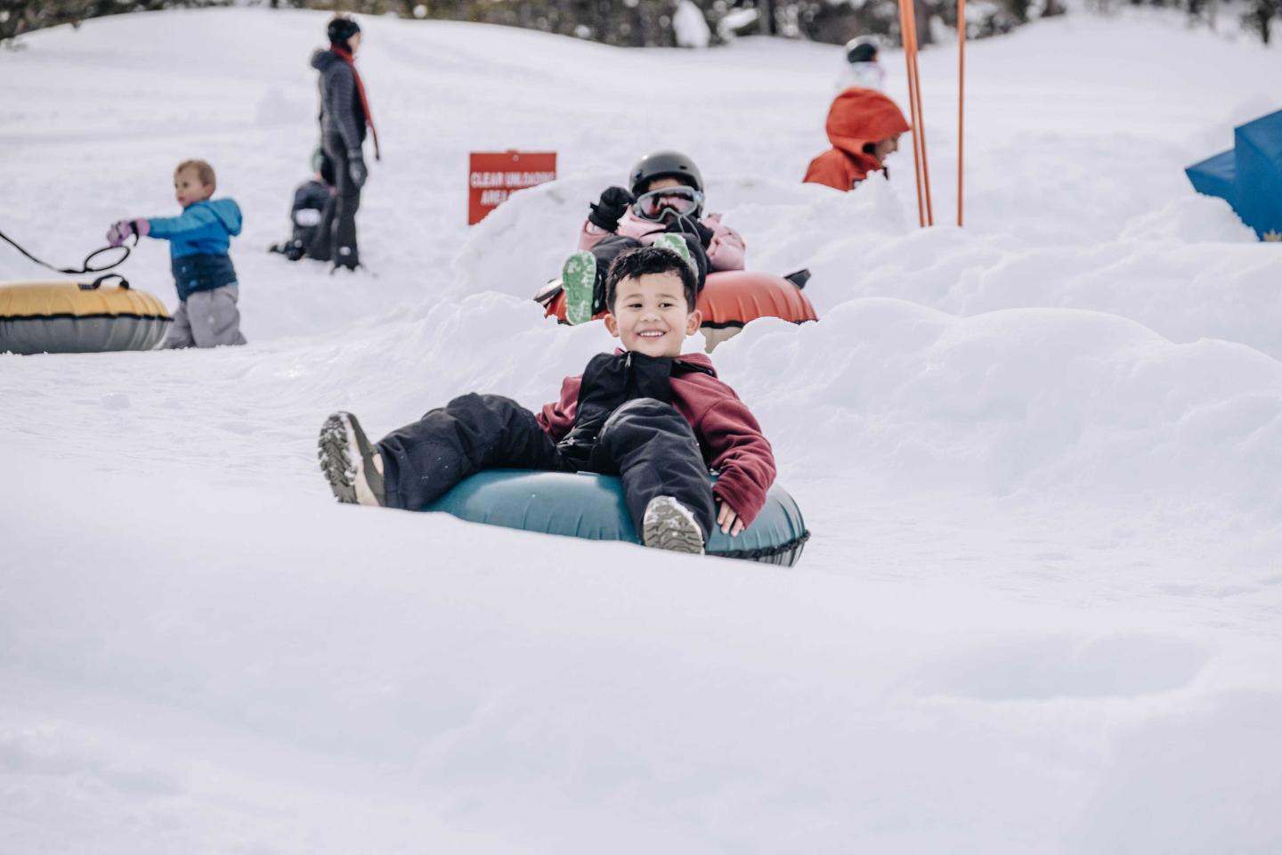 Child snow tubing downhill, smiling in a snowy landscape.