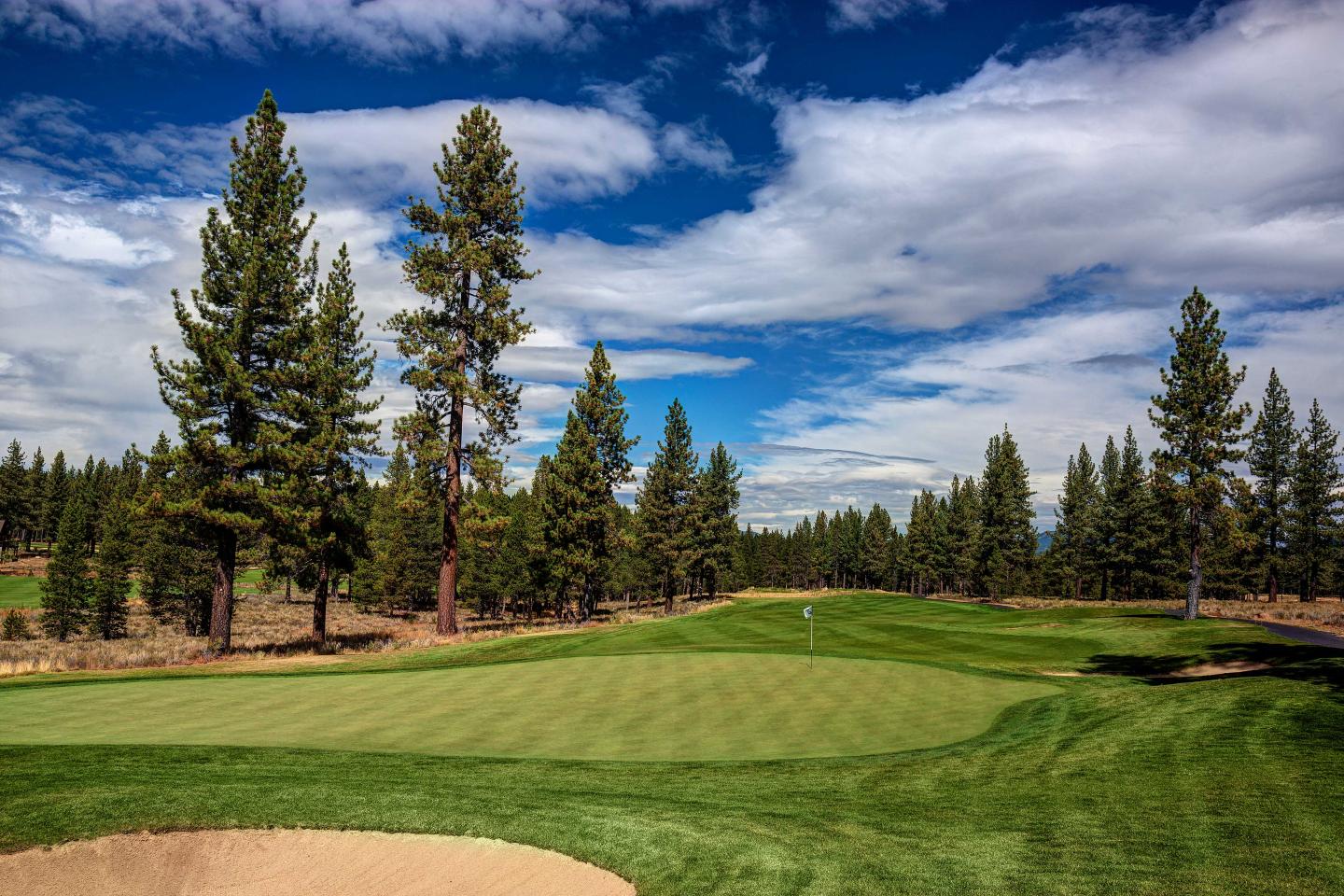 Golf course with lush green grass, sand bunker, trees, and a blue sky.