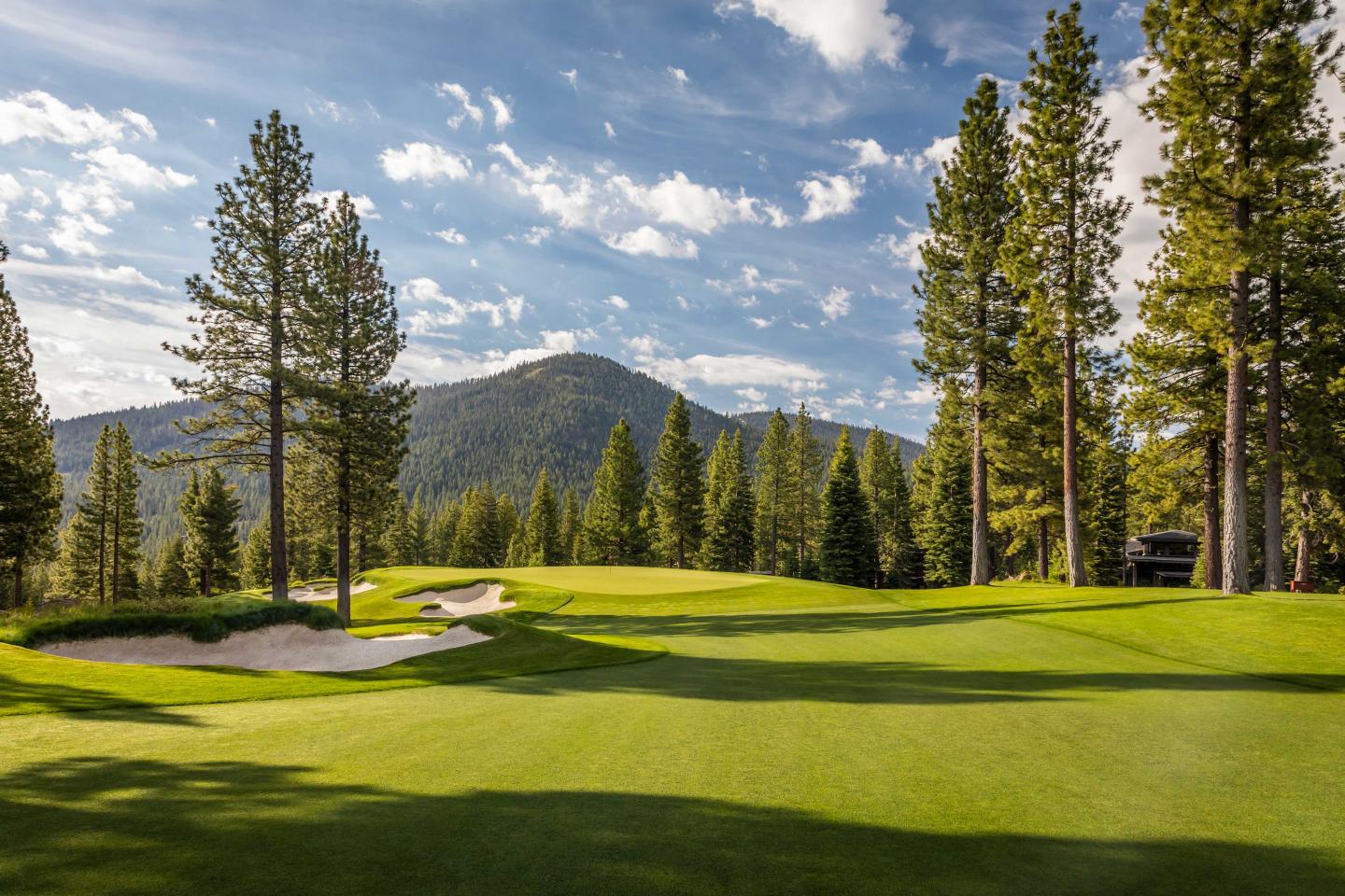 Golf course with trees, mountains, and a blue sky with clouds.