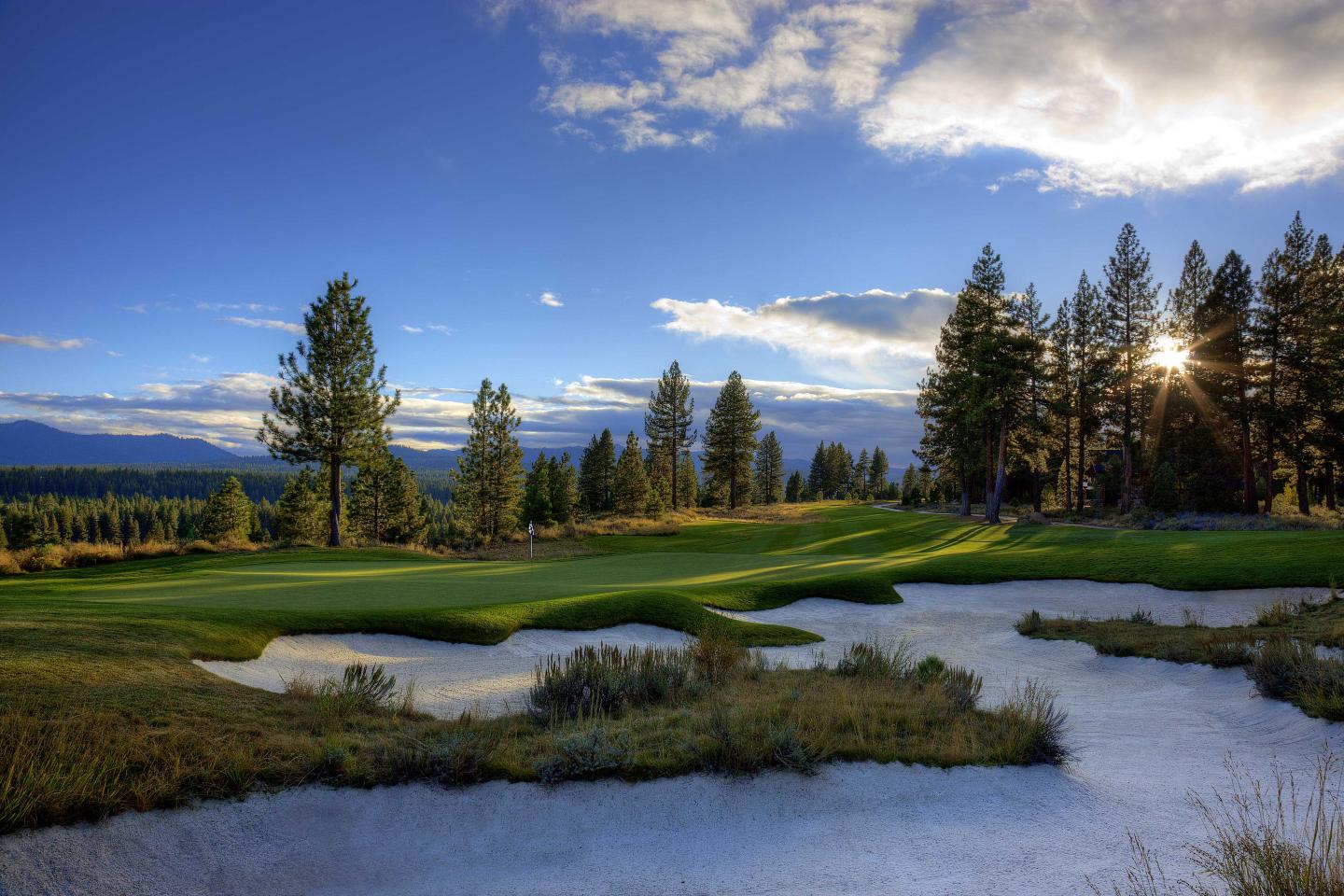 Golf course landscape with sand traps, green fairway, trees, and a bright sky.