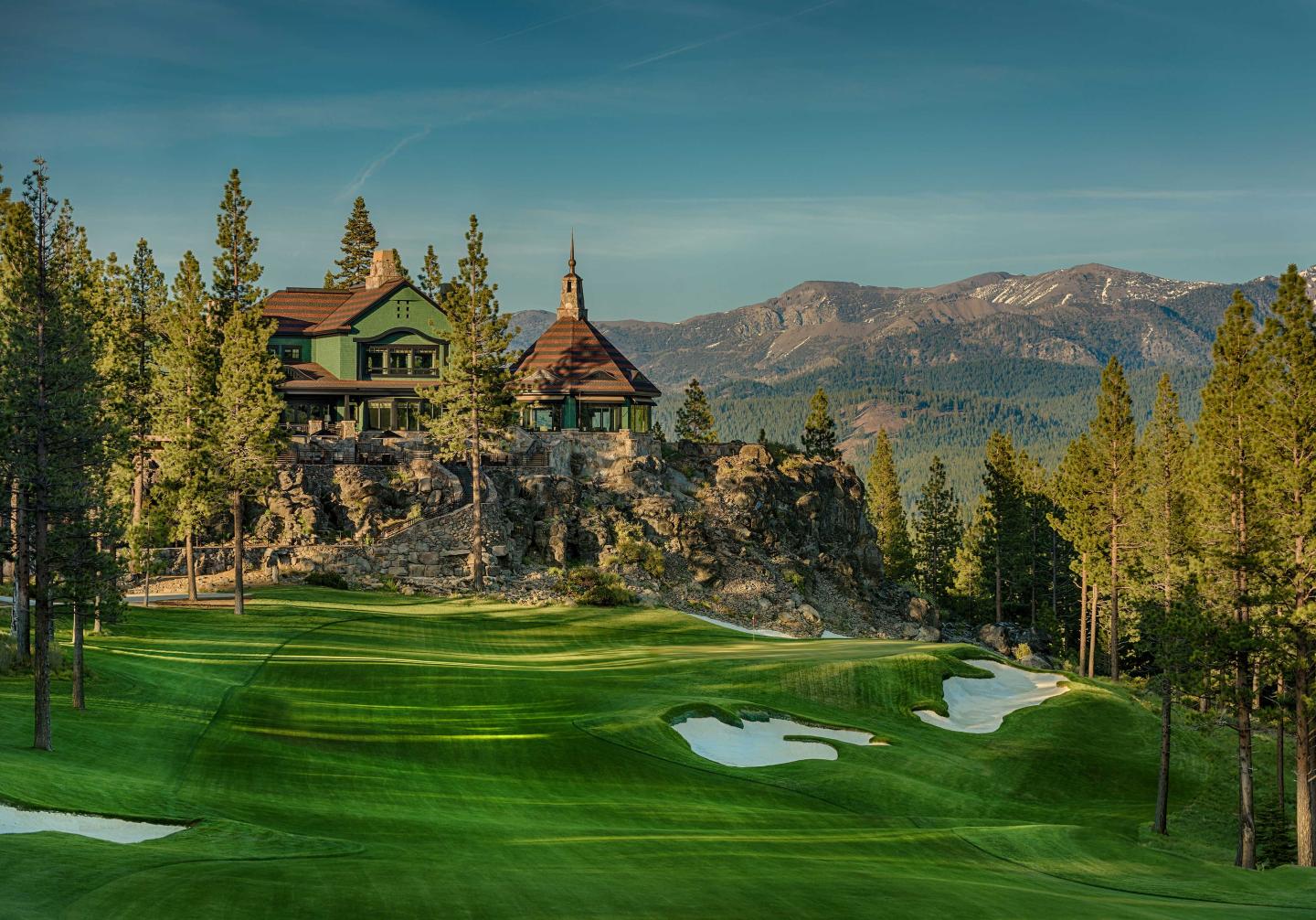 Rustic house on a hill, surrounded by pine trees, overlooking a golf course and mountains.