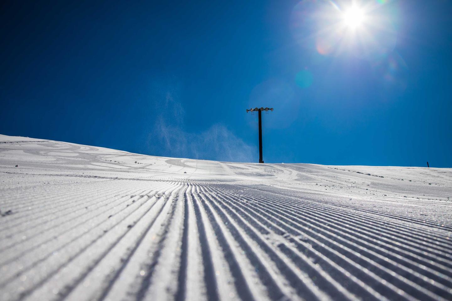 Groomed snowy slope under a bright sun with a clear blue sky.