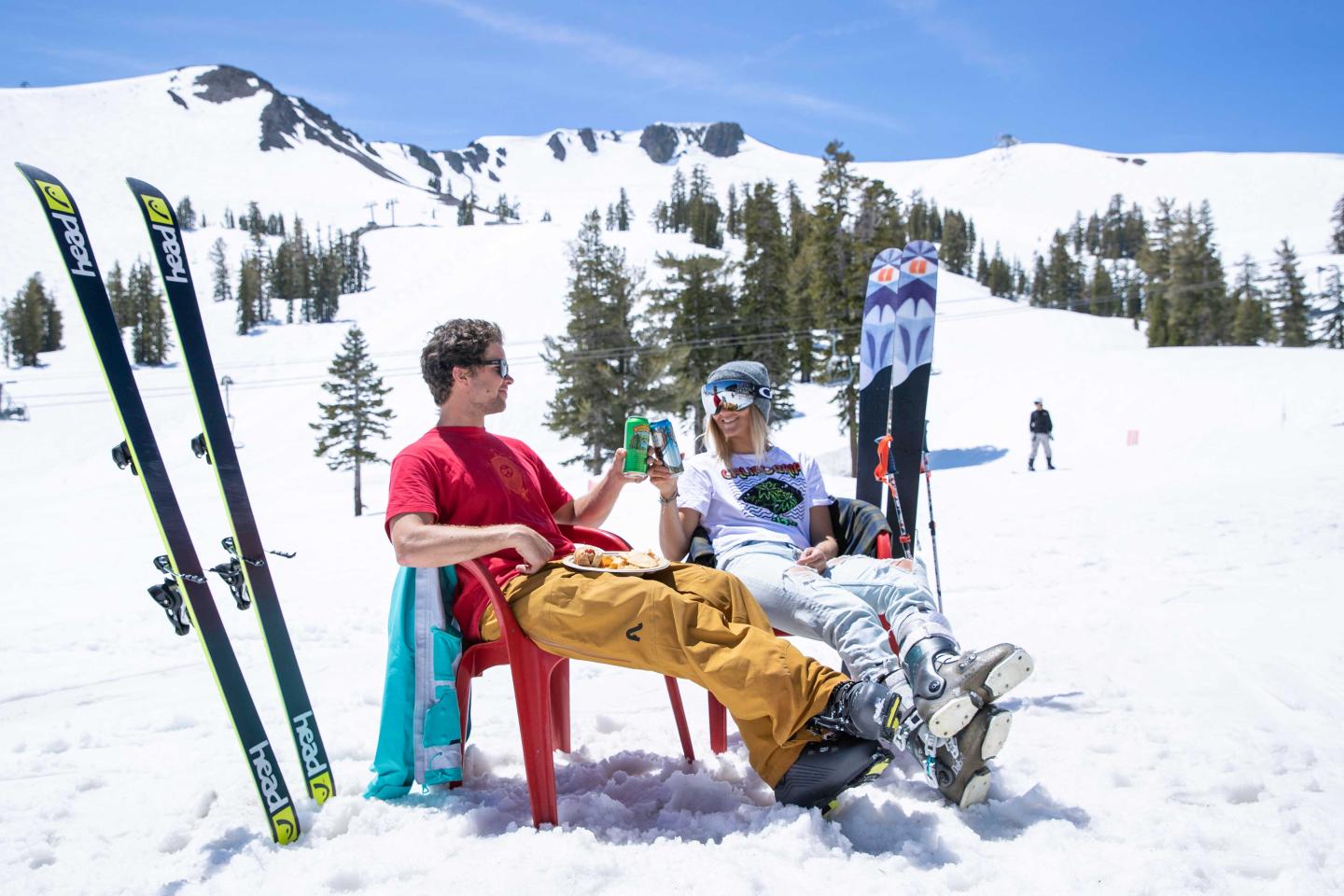 Two skiers relaxing on chairs in snowy mountains under a clear blue sky.