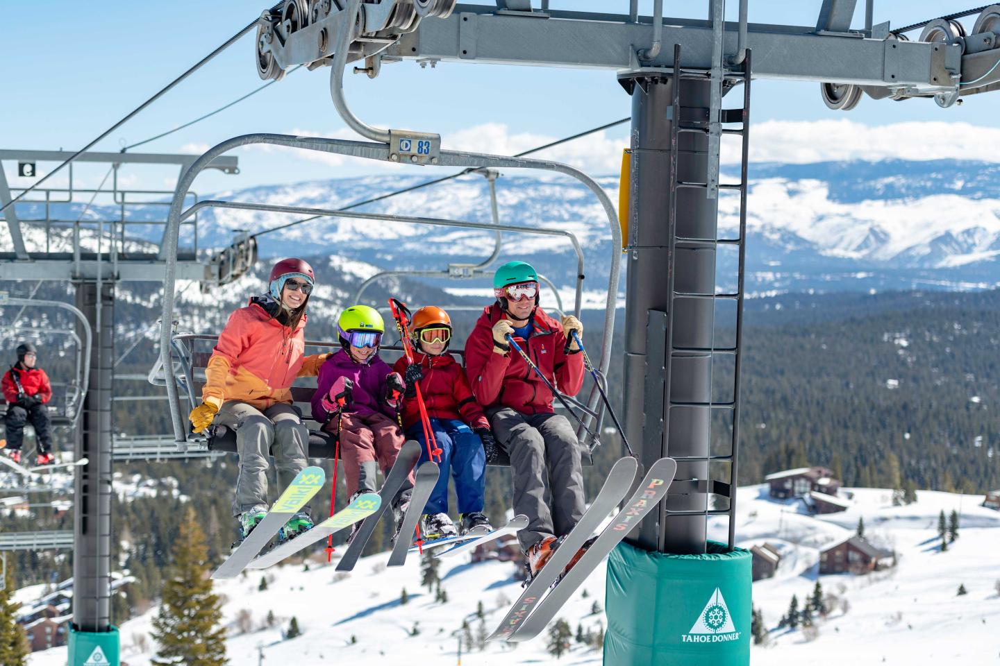 Skiers on a chairlift with snow-covered mountains in the background.