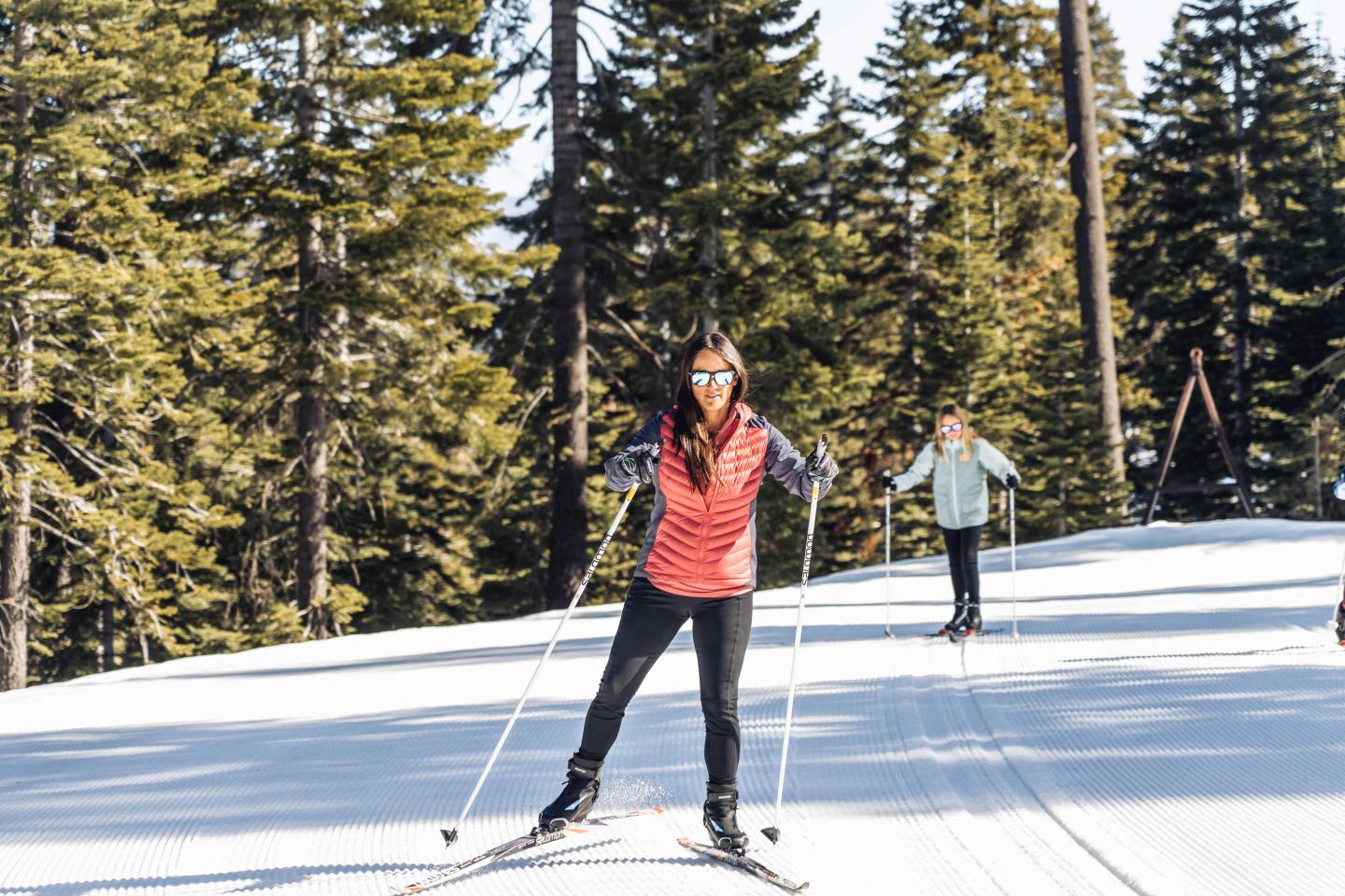 Woman skiing on a snowy slope, surrounded by tall trees.