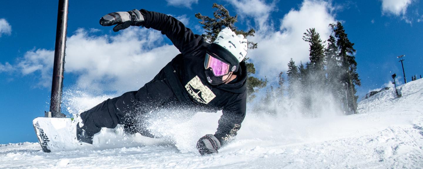 Snowboarder carving down a snowy slope under a clear blue sky.