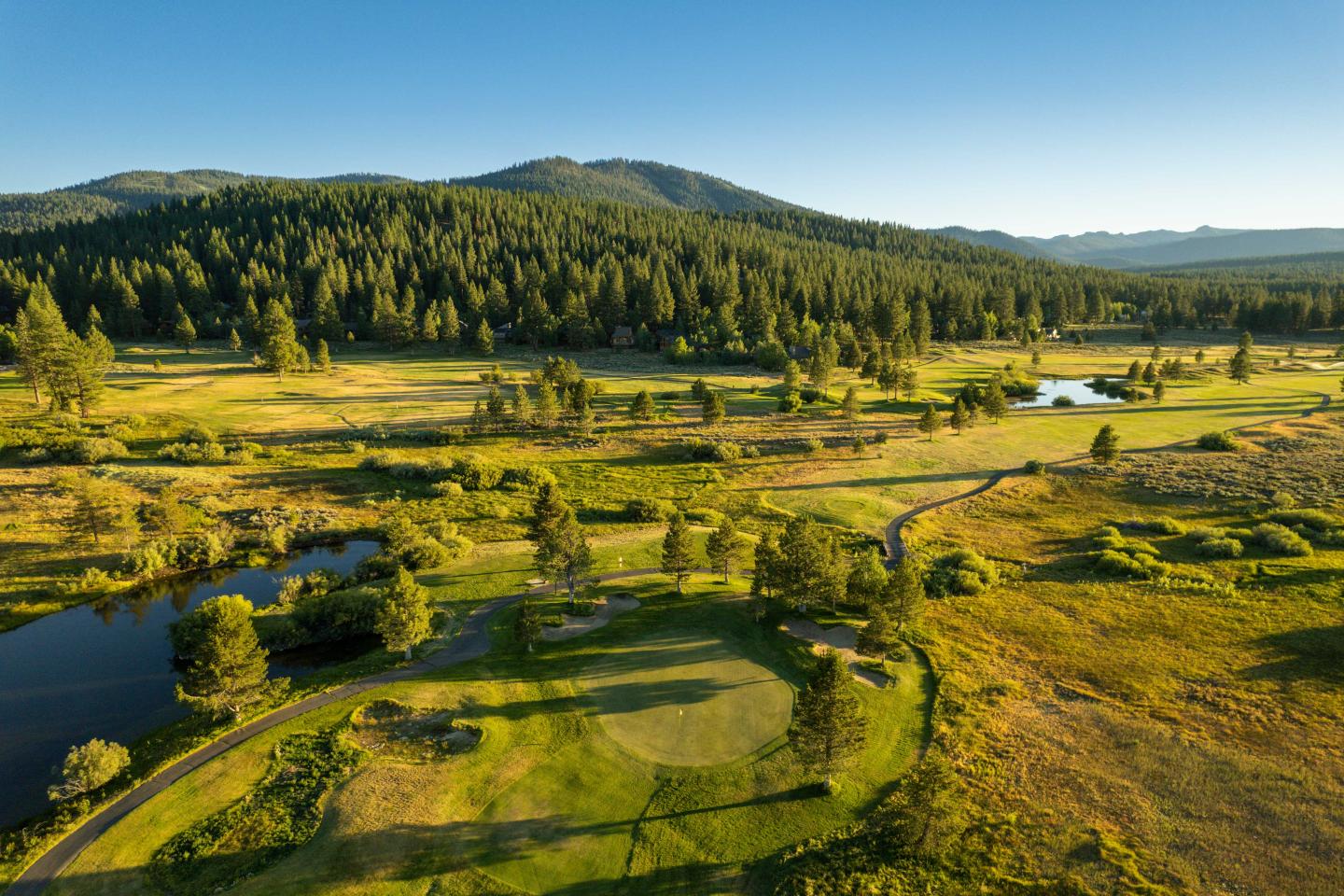 Sunny landscape with a golf course, trees, and distant mountains.