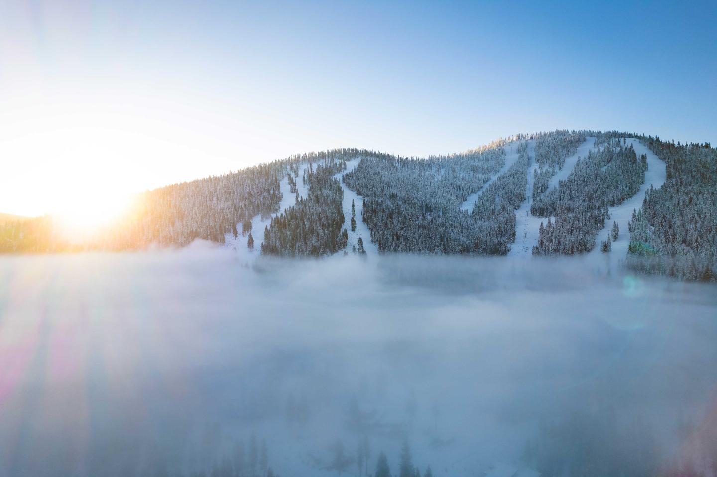 Snowy mountain at sunrise with ski slopes and mist.