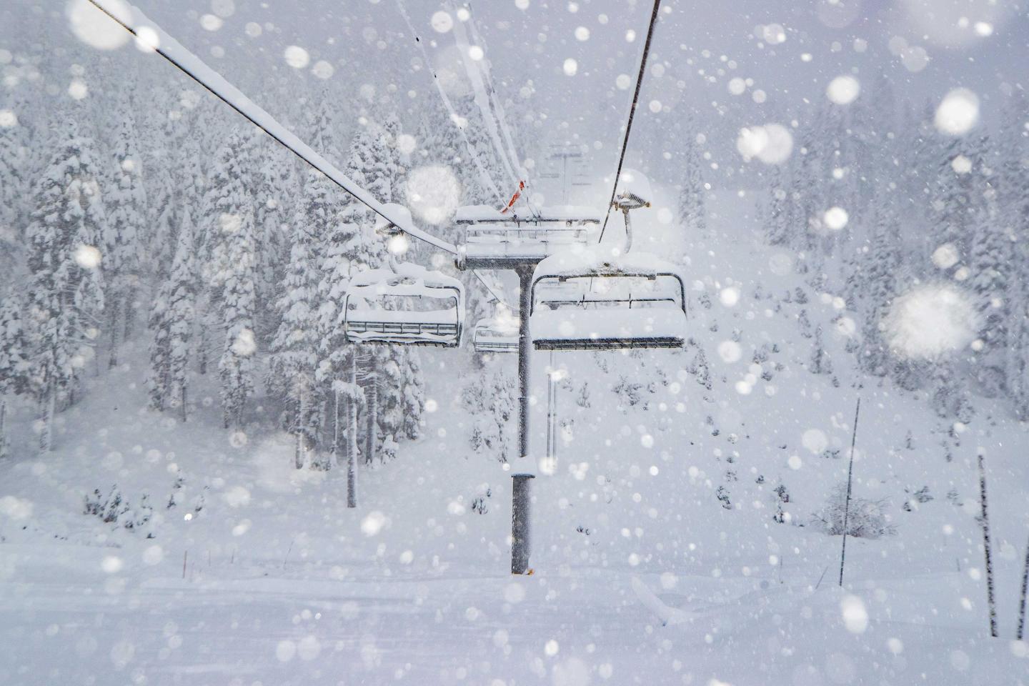 Ski lift in heavy snowfall, snowy forest in background.