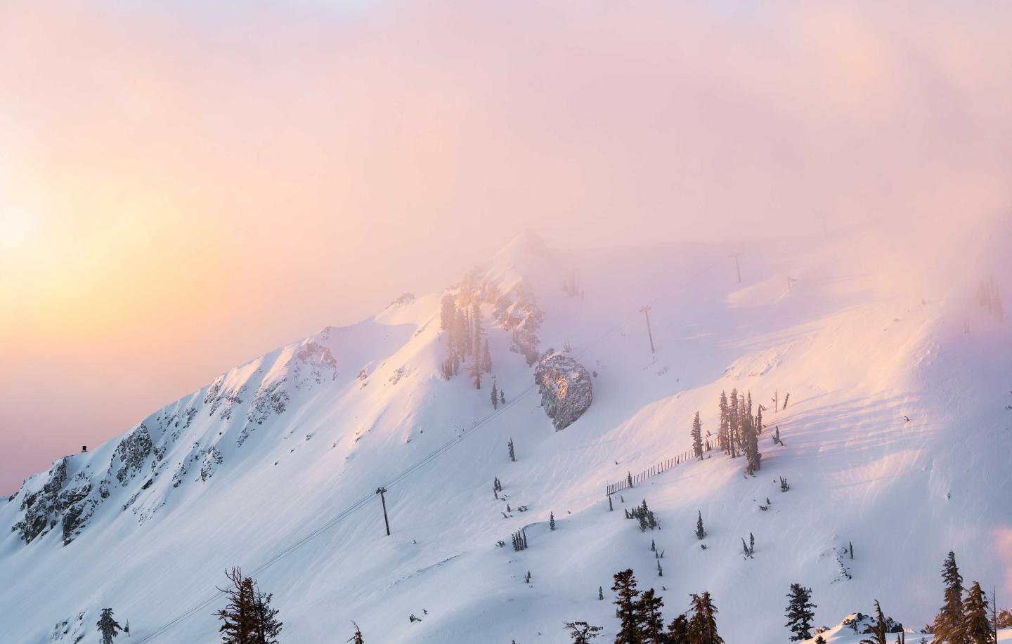 Snowy mountain peak with soft pink and orange sunset sky.