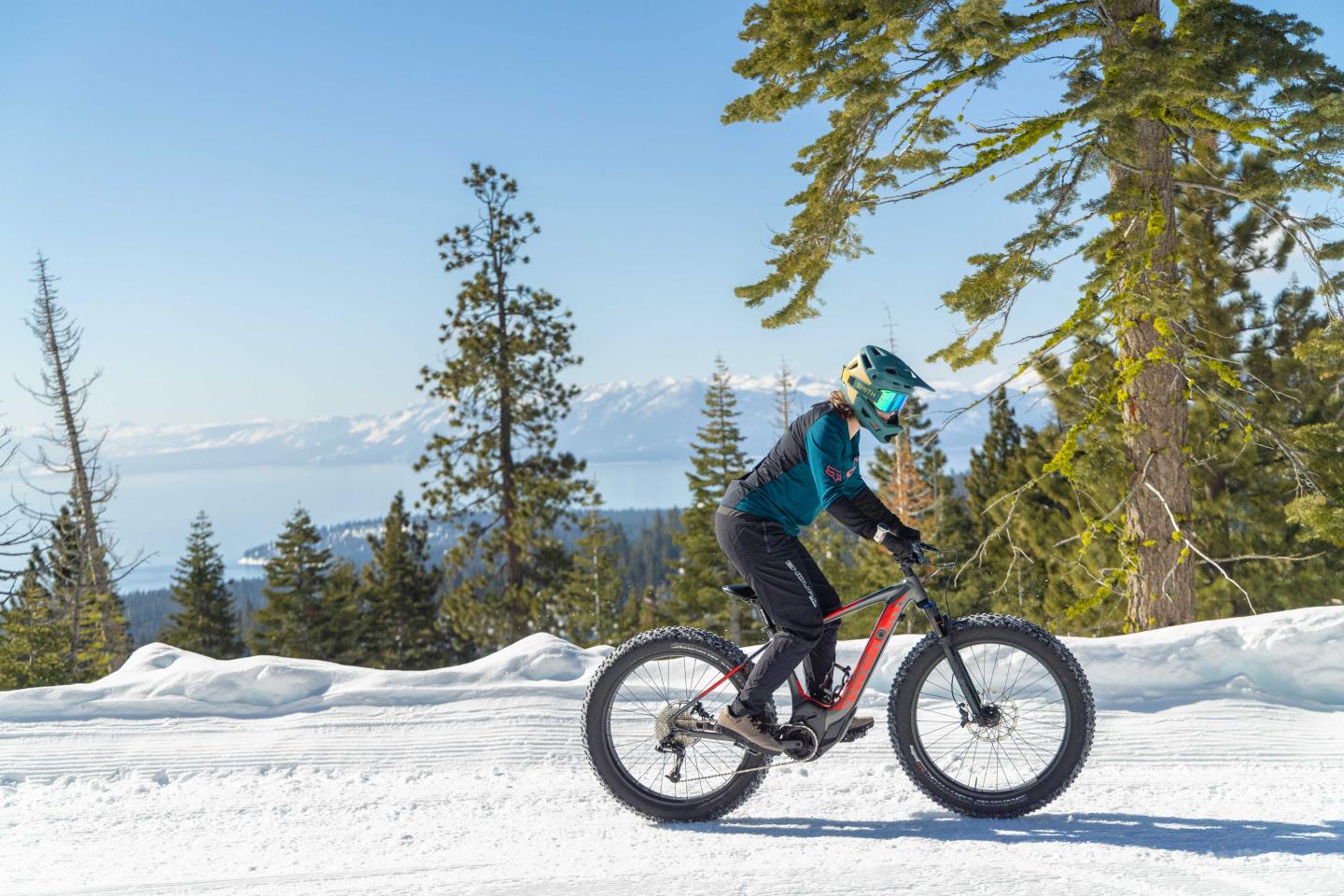 Cyclist riding a fat-tire bike on snowy mountain trail.