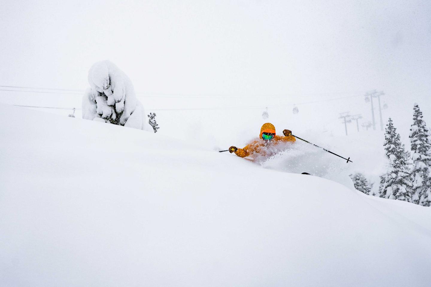 Skier in orange gear glides through deep snow on a snowy mountain slope.