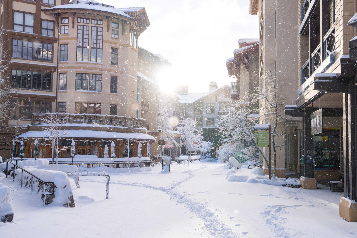 Snowy street between buildings with the sun shining in the background.