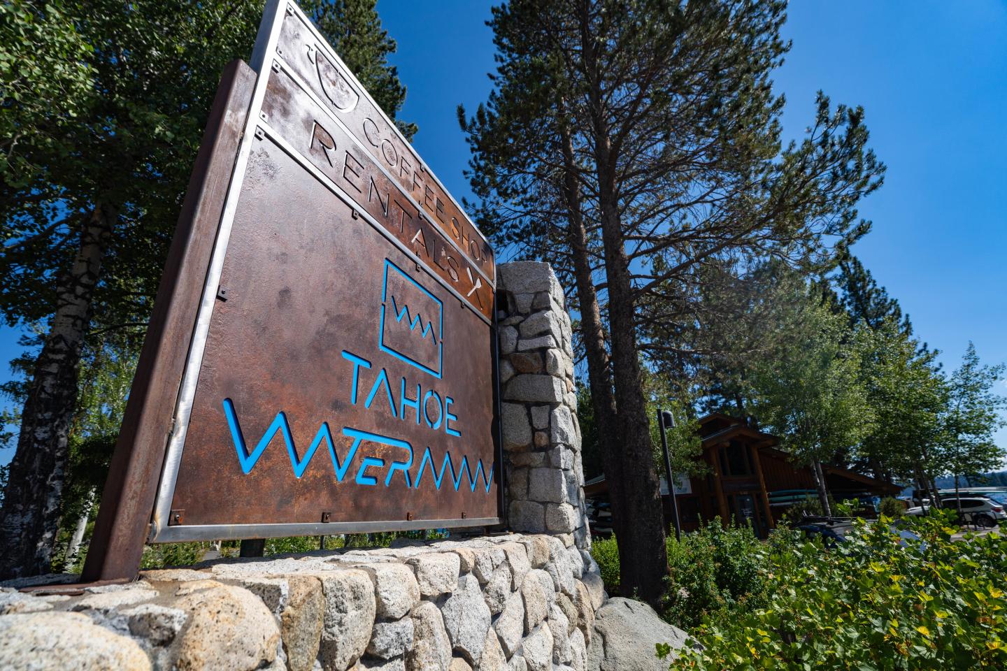 Waterman's Landing Carnelian Bay // Colorful kayaks and paddleboards on a pebble beach by a lake under a clear blue sky.